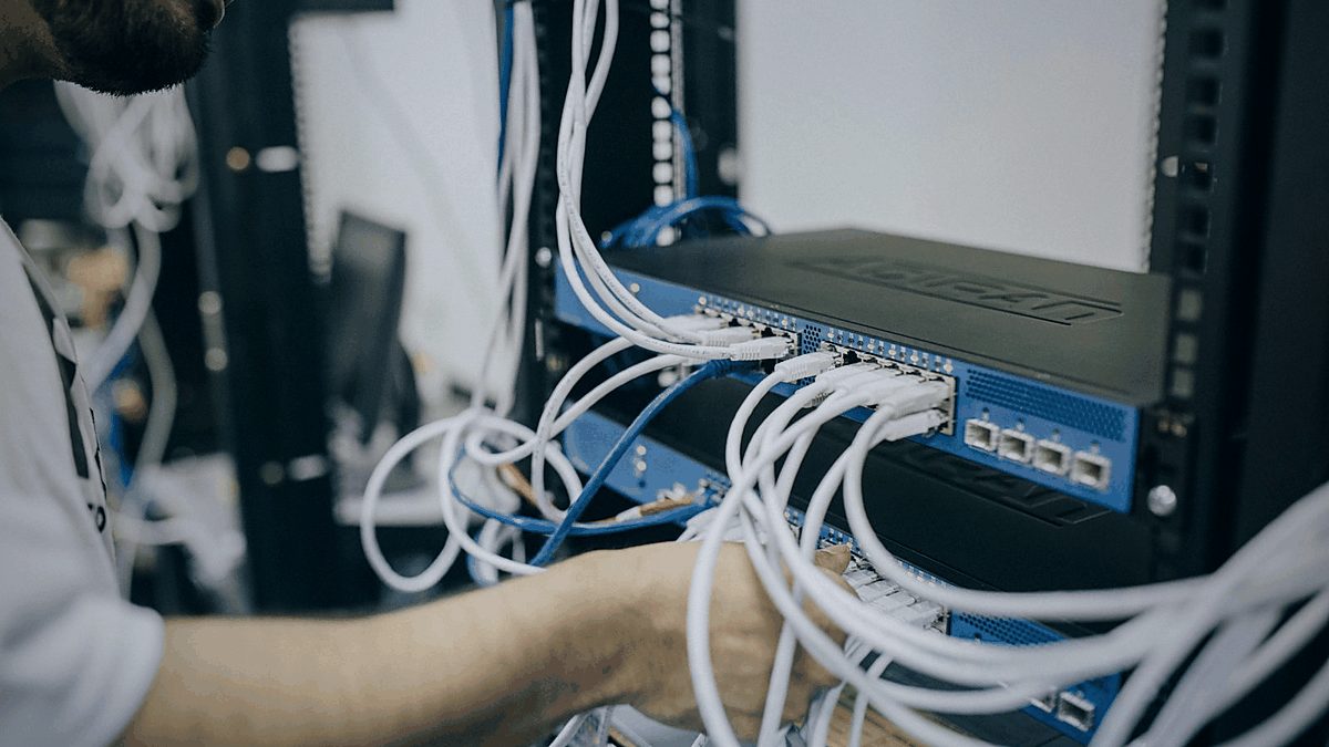 Técnico trabajando en un rack de red con cableado estructurado y equipos de conectividad.